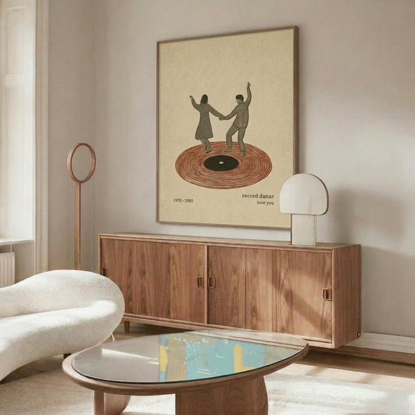 May include: Vintage-style poster print in thin brown frame hanging above wooden mid-century credenza. Artwork shows two silhouetted figures dancing on red vinyl record with cream background and text reading "record danar love you 1970-1980". Room features white curved chair, oval glass coffee table, modern white lamp, and neutral walls with natural lighting.