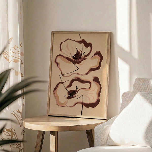 May include: Framed abstract floral artwork featuring two large brown and cream poppies painted in loose, expressive brushstrokes on beige paper, displayed on a round wooden side table next to a beige upholstered chair, with natural sunlight casting geometric shadows across the neutral-toned room and green plant leaves visible in the foreground.