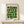 May include: Framed Bauhaus-style poster with geometric green circles and semicircles arranged in a grid pattern on cream background, displayed on light wood surface beside small wrapped gift with twine and dried sprig, against neutral wall with soft natural lighting.