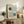 May include: Framed Bauhaus-style poster with geometric design featuring two semi-circular forms in dark green and teal blue with concentric line patterns on cream background, displayed on rustic wooden sideboard alongside books, ceramic vase, and fern plant in modern living room setting with beige chair and neutral decor