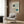 May include: Bauhaus-inspired poster with geometric design featuring curved lines and blue circles on cream background, displayed above modern beige armchair with patterned pillow. Room setting shows wood paneled walls, brass floor lamp, and side table with open book. Minimalist mid-century modern interior styling with warm neutral tones and natural lighting from window.