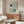 May include: Bauhaus exhibition poster in wooden frame hanging above walnut credenza in modern living room. Poster features geometric design with green and blue circles, curved lines, and "BAUHAUS" text on cream background. Room has white curved chair, glass coffee table, marble floor, and mushroom table lamp.
