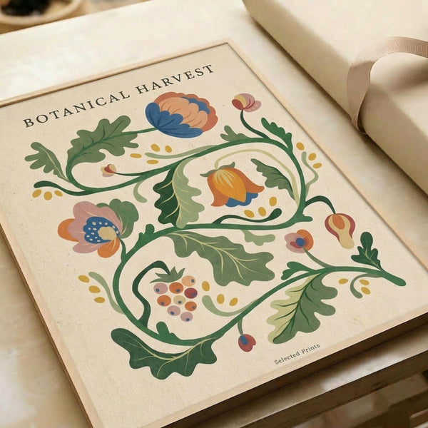 May include: Vintage-style botanical art print with decorative floral design featuring green leafy vines, colorful flowers in blue, orange and pink tones, and small berries. The illustration has an ornate, folk art aesthetic with flowing organic curves on cream-colored paper. Print is shown matted in white frame leaning against neutral colored books or papers in soft natural lighting.