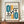 May include: Framed Bauhaus-style poster with geometric shapes in teal, orange, and black on cream background, displayed on wooden sideboard next to white ceramic vase and books in elegant room with white paneled walls