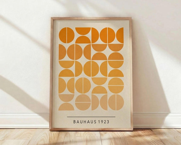 May include: Framed geometric art print featuring orange and yellow circles and semicircles arranged in a grid pattern on cream background, displayed in light wood frame against white wall on wooden floor with natural lighting creating soft shadows