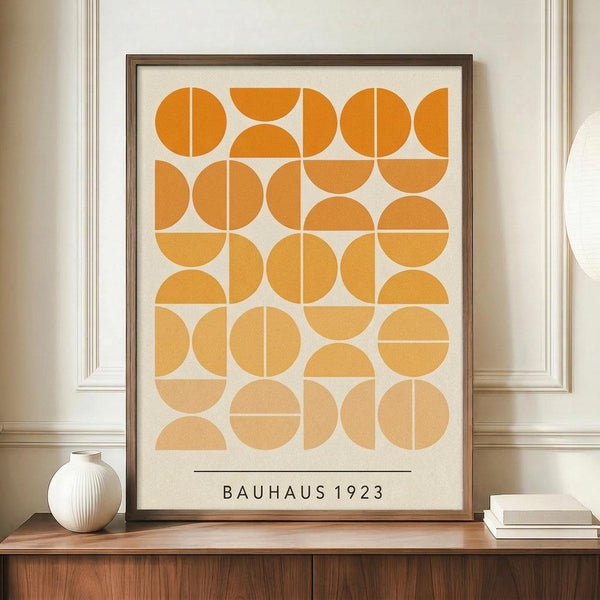 May include: Framed geometric art print with orange and cream circular and semicircular shapes arranged in a grid pattern, displayed on a wooden sideboard next to a small white ribbed vase and stacked books. The print features "BAUHAUS 1923" text at bottom and is set in a brown frame against cream walls with white molding.