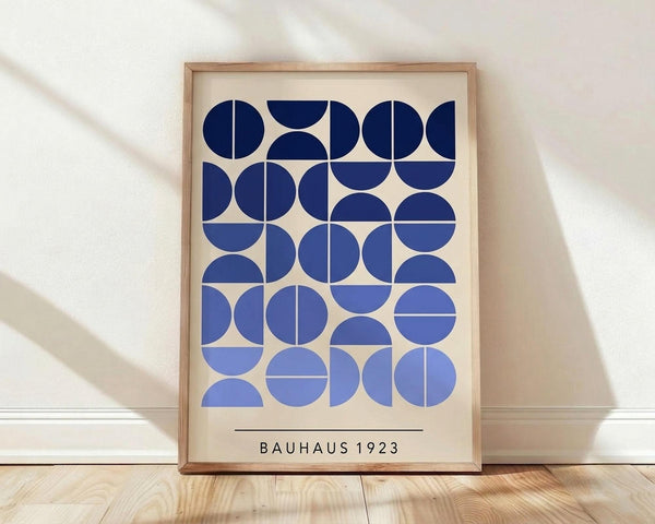 May include: Framed geometric art print with blue circular and semicircular shapes arranged in a grid pattern on cream background, displayed in light wood frame against white wall on wooden floor with natural lighting creating soft shadows