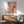 May include: Framed Bauhaus poster with geometric arches in orange and burgundy tones displayed above a mid-century modern wood credenza. Scene features a sage green upholstered armchair with wooden frame, white ceramic table lamp, and warm natural lighting casting shadows on white wall. Mid-century furniture styling with clean lines and warm wood tones throughout the room setting.