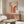 May include: Bauhaus 1923 poster displayed in minimalist living room with warm beige walls. The poster features geometric rainbow arches in orange and burgundy tones on cream background. Room styled with walnut wood credenza, white curved chair, glass oval coffee table, and modern white table lamp. Natural lighting creates soft shadows on polished floors.