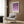 May include: Framed geometric art print featuring purple circles and semicircles in gradient shades from deep violet to light lavender on cream background, displayed above beige upholstered armchair with geometric patterned pillow. Modern reading corner with brass floor lamp, side table with open book, and warm wood paneled walls.