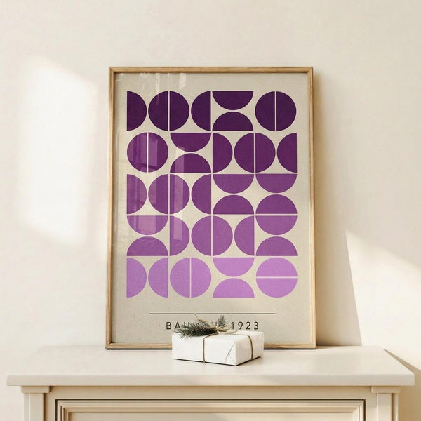 May include: Framed geometric art print with purple and lavender circles arranged in a grid pattern on cream background, displayed on light wood console table next to small wrapped gift with natural twine and greenery sprig against white wall