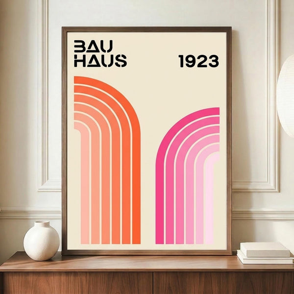 May include: Framed geometric poster with cream background featuring orange and pink curved rainbow stripes, black "BAUHAUS 1923" text at top, displayed on wooden sideboard next to white ceramic vase and books in elegant room with white paneled walls.