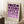 May include: Framed geometric art print with purple circles and semicircles arranged in a grid pattern on cream background, displayed leaning against white wall corner. Print shows "BAUHAUS 1923" text at bottom. Scene includes wooden side table with white coffee cup and saucer, textured cream rug, and soft natural lighting creating shadows on the wall.