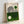 Framed Bauhaus-style poster with geometric design featuring black concentric lines forming curved shapes on cream and green color-blocked background. Two circles - one dark green, one cream - accent the composition. Text reads "BAUHAUS" at top and "Ausstellung Juli - Sept 1923" at bottom. Light wood frame leaning against white wall.