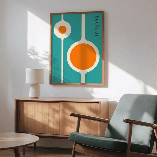 May include: Framed mid-century modern poster with turquoise background featuring white geometric shapes and orange circles resembling kitchen utensils, displayed above wooden sideboard with white ceramic lamp in minimalist living room with sage green upholstered chair and natural lighting creating diagonal shadows on white wall