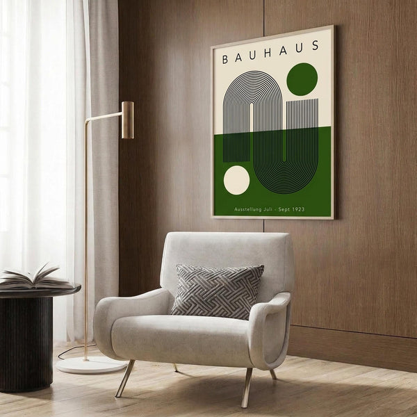 May include: Bauhaus-style poster with green and cream geometric design featuring concentric arcs and circles, displayed in light wood frame on wooden wall panel. Modern beige armchair with geometric pillow, brass floor lamp with white base, and dark round side table with open book create contemporary living room setting with natural lighting from window.