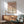 May include: Framed geometric poster with warm terracotta, beige and cream circular shapes arranged in a grid pattern, displayed above a mid-century wooden credenza with sliding doors. Scene shows mint green upholstered armchair with wooden frame, white ceramic table lamp, and natural sunlight casting shadows across white walls in a modern living room setting.