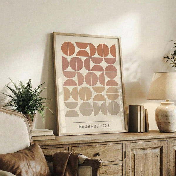 May include: Framed geometric art print featuring circles and semicircles in warm terracotta, rust, and beige tones arranged in a grid pattern, displayed on rustic wooden sideboard alongside fern plant, books, ceramic vase, and tan leather chair in naturally lit living room with cream walls.