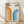 May include: Framed geometric poster with cream background displaying "BAUHAUS 1923" text and two curved rainbow stripe designs - orange gradient arcs on left, blue gradient arcs on right. Light wood frame sits on wooden floor against white wall with soft natural lighting casting diagonal shadows.