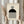 May include: Person holding framed Bauhaus poster with geometric design featuring concentric circles, black semicircle, and vertical black stripes on cream background. Light wooden frame, neutral beige clothing, dried pampas grass, soft natural lighting against white curtained window.