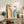 May include: Framed Bauhaus poster with orange and blue geometric arches on cream background, displayed on rustic wooden sideboard alongside fern plant, stacked books, ceramic vase, and leather chair in neutral-toned living room setting