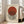 May include: Framed Bauhaus-style poster print featuring a rust-colored circle overlapping black and white vertical stripes on cream background, displayed in light wood frame leaning against white wall corner next to beige upholstered sofa in bright, naturally-lit room with hardwood floors and white area rug.