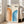 May include: Framed Bauhaus-inspired poster with orange and blue geometric rainbow arches on cream background, displayed in bright living room with beige sofa, white walls, and natural light from windows. Modern minimalist art print in light wood frame leaning against wall on hardwood floor.
