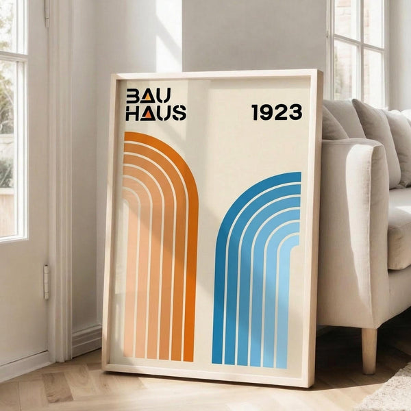 May include: Framed Bauhaus-inspired poster with orange and blue geometric rainbow arches on cream background, displayed in bright living room with beige sofa, white walls, and natural light from windows. Modern minimalist art print in light wood frame leaning against wall on hardwood floor.