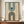 May include: Framed geometric poster with two arch designs in teal blue and brown on cream background, displayed on wooden credenza beside white ceramic vase and stacked books in elegant room with white paneled walls