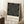 May include: A framed geometric art print leaning against a white wall, featuring black background with white curved parallel lines forming abstract shapes. Light wood frame, displayed beside a coffee cup on wooden block and cream blanket. Natural lighting creates soft shadows on the wall.