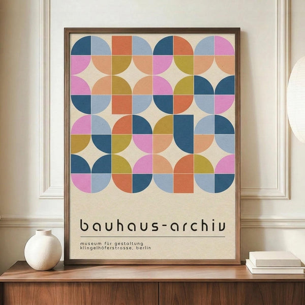 May include: Framed geometric art print with colorful circles and squares in pink, blue, orange, and green tones, displayed on wooden sideboard next to white ceramic vase and books in room with white paneled walls