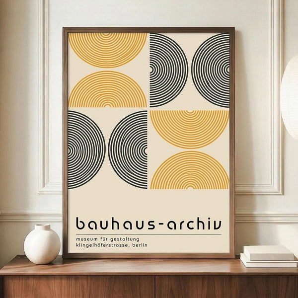 May include: Framed poster with geometric design featuring orange and black concentric semicircles and circles arranged in a grid pattern on cream background, displayed on wooden sideboard next to white ceramic vase and stacked books in elegant room with white wainscoting