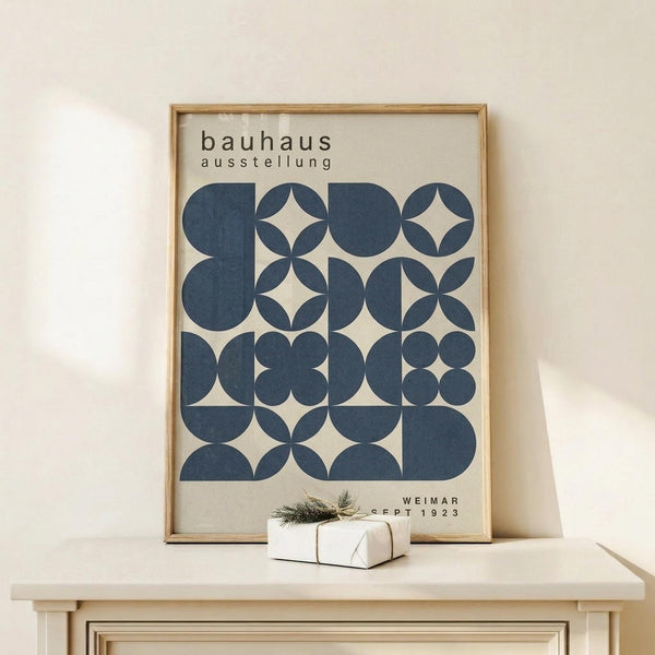 May include: Framed poster with dark blue geometric circles and semicircles arranged in a grid pattern on cream background, displayed on light wood console table with small wrapped gift beside it, against white wall with natural lighting casting soft shadows.