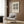 May include: Beige and cream framed Bauhaus poster with black geometric pattern of circles, triangles and diamonds mounted on wood paneled wall above modern light gray armchair with patterned pillow, brass floor lamp and dark round side table with open book in minimalist room setting