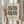 May include: Person in beige sweater holding framed geometric poster with black triangles and circles on cream background, dried pampas grass beside them, neutral curtained window setting, light wood frame