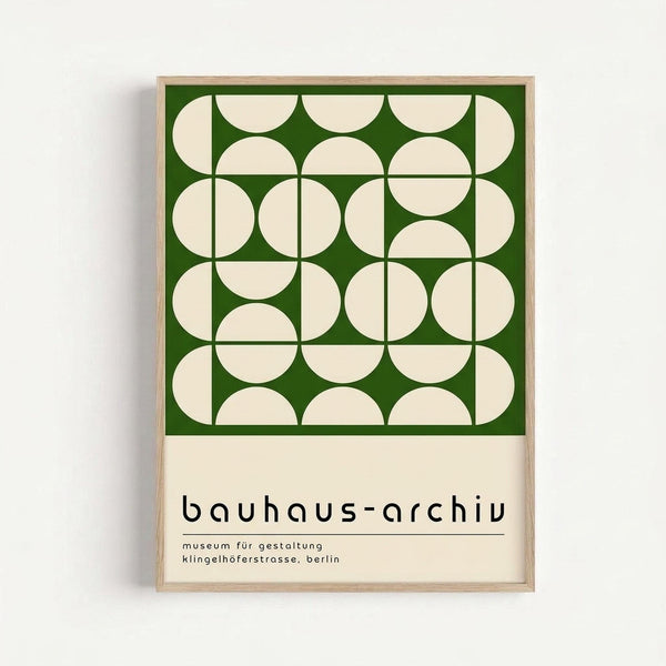 Framed geometric poster with green background featuring cream-colored overlapping circles and rounded rectangles in a grid pattern. Text below reads "bauhaus-archiv" and "museum für gestaltung klingelhöferstrasse, berlin" in black lowercase letters. Light wood frame against white wall background.