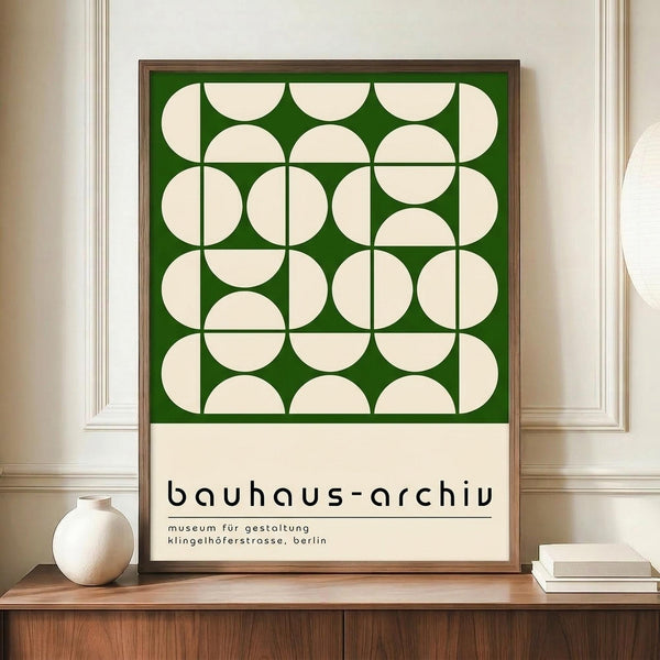 May include: Framed Bauhaus-style poster with green background and cream geometric circles pattern, displayed on wooden sideboard next to white ceramic vase and books in elegant room with white paneled walls