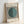 May include: Framed Bauhaus exhibition poster leaning against white wall. Design features black and white vertical stripes with teal green circle overlay. Text reads "bauhaus ausstellung" at top and "WEIMAR JULI-SEPT 1923" at bottom. Light wood frame, minimalist modernist aesthetic with geometric pattern creating optical illusion effect.