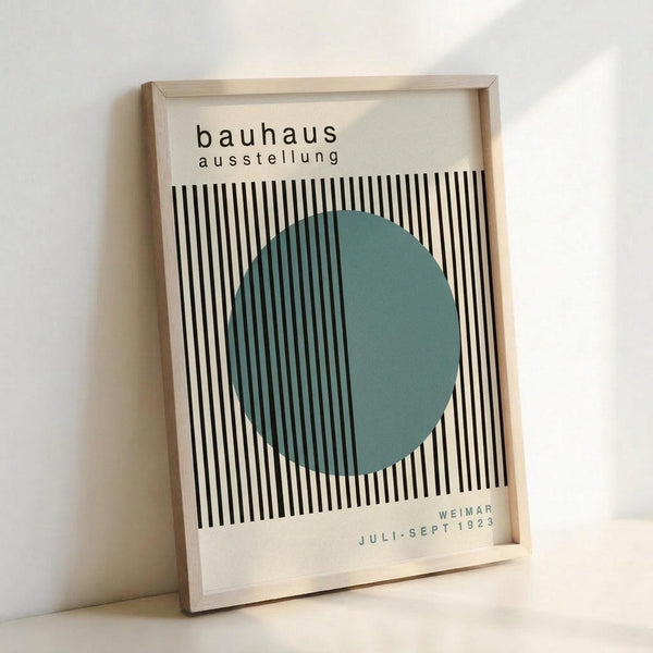 May include: Framed Bauhaus exhibition poster leaning against white wall. Design features black and white vertical stripes with teal green circle overlay. Text reads "bauhaus ausstellung" at top and "WEIMAR JULI-SEPT 1923" at bottom. Light wood frame, minimalist modernist aesthetic with geometric pattern creating optical illusion effect.