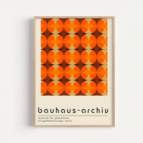 A framed poster featuring a geometric pattern of overlapping orange circles creating an interlocking design in warm tones of bright orange, burnt orange, and cream. The repeated circular motifs form diamond-shaped negative spaces in brown. Below the pattern is black text reading "bauhaus-archiv" followed by smaller text "museum für gestaltung" and "klingelhöferstrasse, berlin" on a cream background. The poster is displayed in a light wood frame against a white wall.