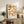 May include: Framed colorful geometric poster with overlapping semicircles in vibrant hues of yellow, orange, pink, blue, teal, and green on cream background, displayed on rustic wood sideboard alongside potted fern, ceramic vases, and books in cozy living room with beige armchair and neutral walls.