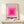 May include: Framed poster with pink concentric squares creating an ombre effect from deep magenta center to pale pink outer edge, displayed on light wood shelf against cream wall. Small white wrapped gift with twine and evergreen sprig sits beside the thin wooden frame. The minimalist geometric design features bold black text below the squares.