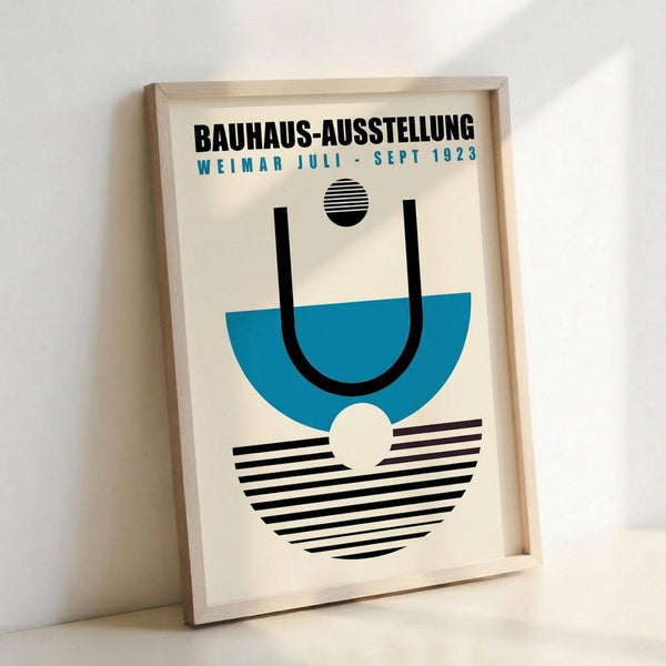 Bauhaus-style poster in light wood frame leaning against white wall. Features geometric design with black and blue semicircles, striped elements, and bold typography reading "BAUHAUS-AUSSTELLUNG WEIMAR JULI-SEPT 1923" in black and teal text on cream background.