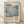 May include: Framed art print featuring Mark Rothko's name in large serif text above an abstract composition of soft gray and blue rectangular color blocks. Below shows "Rothko" and "1903-1970" with descriptive text about the artist. The beige poster has a light wood frame and leans against a white textured wall on wooden flooring, with natural shadows cast across the scene.