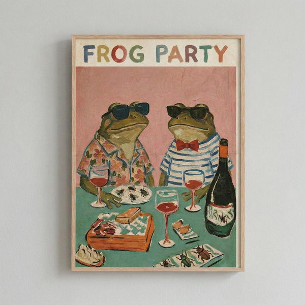 Framed poster artwork showing two anthropomorphic frogs wearing sunglasses seated at a turquoise table. The left frog wears a floral Hawaiian shirt, the right wears a striped shirt with red bow tie. The table displays wine glasses filled with red wine, a wine bottle, plates of insects, and various appetizers. The background is coral pink, with "FROG PARTY" text at the top in colorful block letters. The artwork has a whimsical, painted style in a light wooden frame.