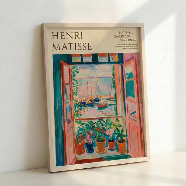 May include: Framed vintage art exhibition poster featuring Henri Matisse's colorful Fauve painting of an open window view. The artwork shows potted plants on a windowsill overlooking boats in a harbor, painted in vibrant blues, oranges, pinks and greens. Light wood frame displays the cream-colored poster against a white wall, showing the National Gallery of Modern Art branding in the upper right corner.