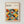 May include: Framed poster with geometric pattern of overlapping circles in orange, yellow, teal, olive green, and gray colors creating a repeating grid design. Text reads "BAUHAUS Modernism, minimalism & abstract arts 1919-1933" and "School of Architecture Weimar, Dessau, Berlin". Light wood frame hangs on white textured wall.