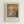 May include: Framed art print in light wood frame on white wall showing Impressionist-style painting of beach sunset scene with golden sun reflecting on water, solitary figure walking on sandy shore, warm orange and yellow sky. French text below reads "ART CONTEMPORAIN INSPIRÉ PAR UN MAÎTRE ARTISTIQUE" and "MONET" in large letters. White matting surrounds artwork.