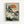 May include: Japanese woodblock print artwork displayed in light wood frame on white wall, featuring white cranes or herons among pine trees beside water, with orange sun in background and Japanese text in upper left corner, rendered in traditional ukiyo-e style with muted colors of teal, orange, and cream