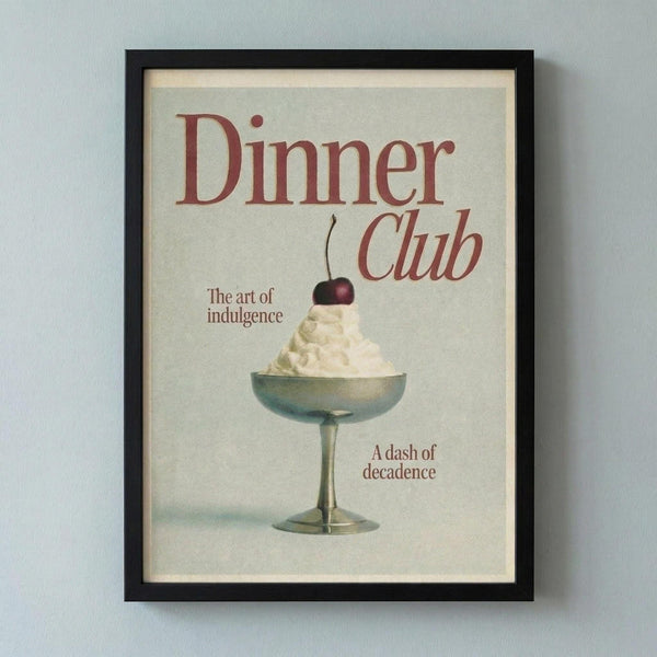 May include: Black framed vintage-style poster print hanging on white wall featuring cream-colored dessert with cherry on top in glass pedestal bowl. Red text reads "Dinner Club" with "The art of indulgence" and "A dash of decadence" in smaller burgundy lettering. Muted beige background with retro aesthetic.